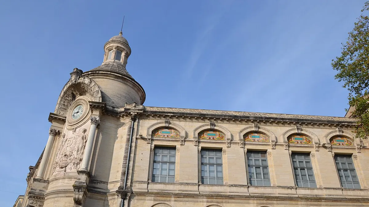 La rotonde d'angle du lycée Alphonse Daudet, avec son horloge, ses colonnes et son dôme, et la façade en pierre blonde ornée de frises de céramique colorée au-dessus des fenêtres.