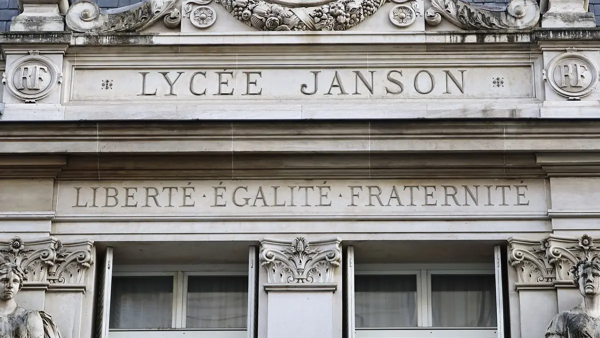 Photo en gros plan : le fronton sculpté de l'entrée, avec l'inscription « Lycée Janson » et en dessous la devise « Liberté Égalité Fraternité », surmontés d'une horloge.