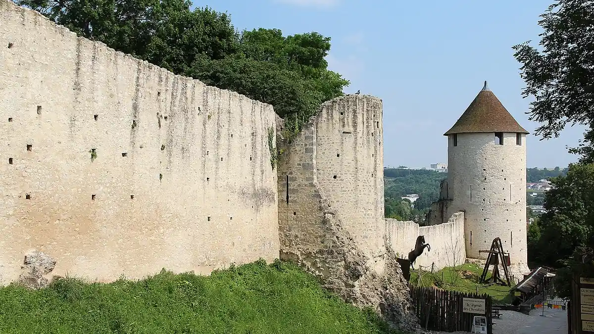 Les remparts médiévaux de la ville haute de Provins : un long mur de pierre claire et une tour ronde à toit pointu, sous un ciel d'été.