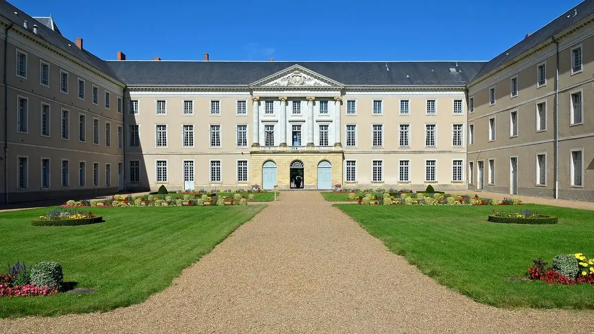 La cour d'honneur du Prytanée national militaire à La Flèche : une longue façade classique en tuffeau clair avec un pavillon central à fronton, des toits d'ardoise, des pelouses et des parterres fleuris.