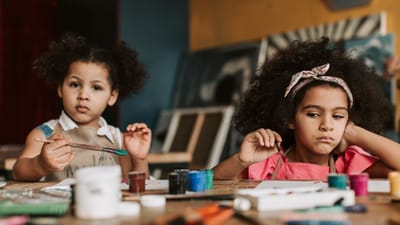 Deux jeunes filles peignant avec des aquarelles dans un cadre de cours d'art intérieur, mettant l'accent sur la créativité.