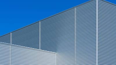 Façade minimaliste d'un bâtiment moderne avec texture métallique contre un ciel bleu.
