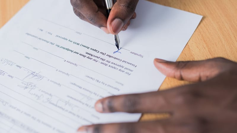 Vue en gros plan de la main d'une personne signant un contrat commercial sur un bureau avec un stylo.