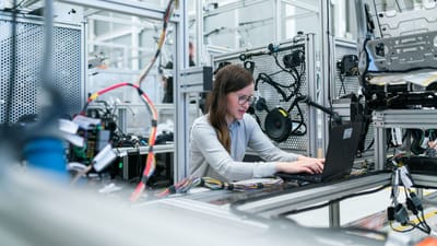 Une ingénieure se concentre sur son ordinateur portable au milieu d'équipements technologiques avancés dans un laboratoire.