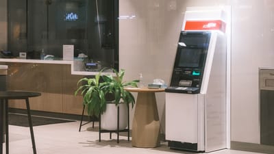 Un distributeur automatique se trouve dans un hall de banque moderne, à côté d'une plante et d'une table.