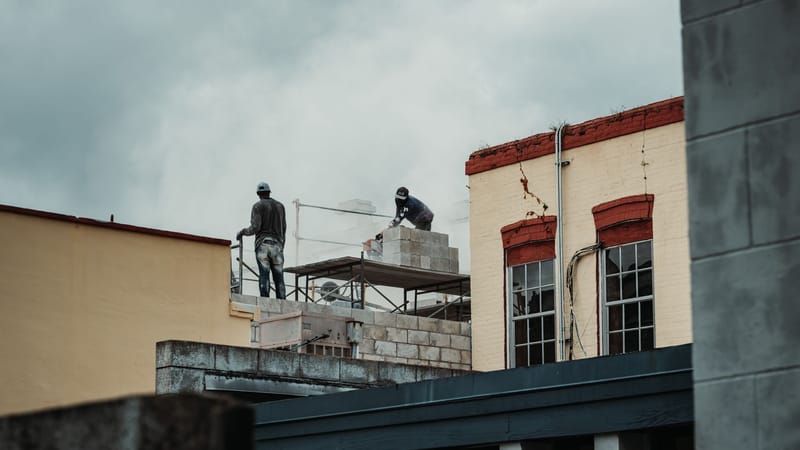 Scène de construction urbaine avec des travailleurs posant des briques sur un site, capturée pendant la journée.