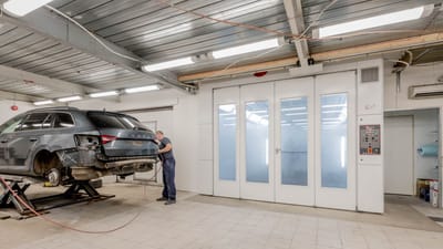 Mécanicien réparant une voiture à l'intérieur d'un atelier automobile, se concentrant sur l'entretien du véhicule.