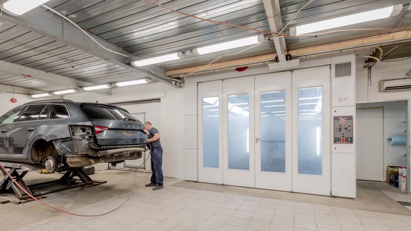 Mécanicien réparant une voiture à l'intérieur d'un atelier automobile, se concentrant sur l'entretien du véhicule.