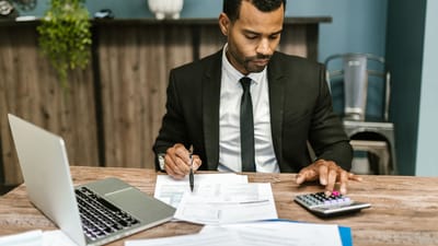 Un homme d'affaires concentré travaille avec une calculatrice et des documents dans un bureau moderne.