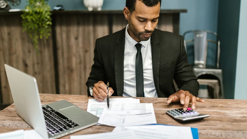 Un homme d'affaires concentré travaille avec une calculatrice et des documents dans un bureau moderne.