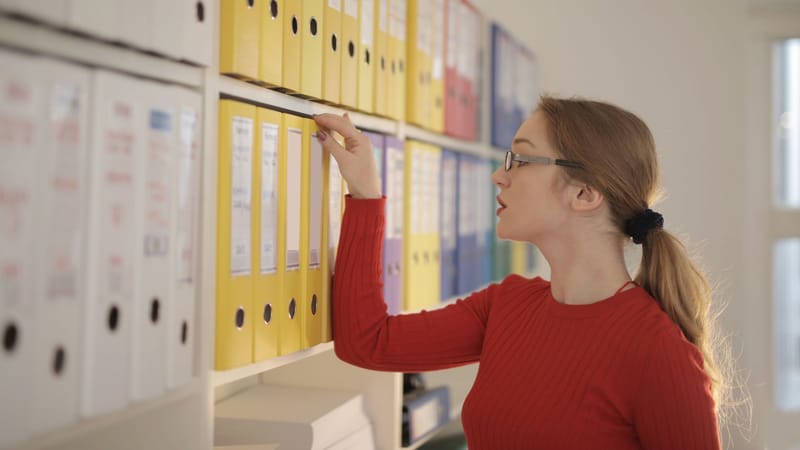 Une femme concentrée dans son bureau, organisant et cherchant à travers des classeurs colorés.