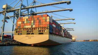 Un grand porte-conteneurs dans un port industriel avec des grues sous un ciel bleu clair.