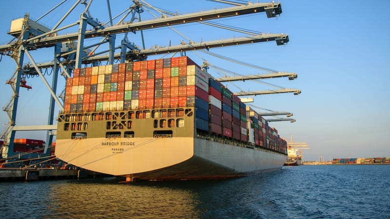 Un grand porte-conteneurs dans un port industriel avec des grues sous un ciel bleu clair.
