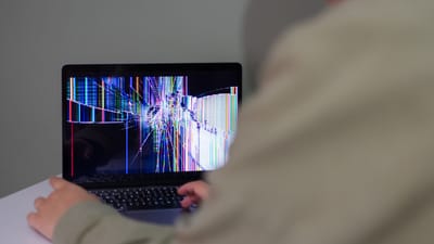 Une personne interagit avec un ordinateur portable qui a un écran fissuré et déformé.