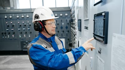 Technicien en équipement de sécurité travaillant sur un panneau de contrôle industriel à l'intérieur.