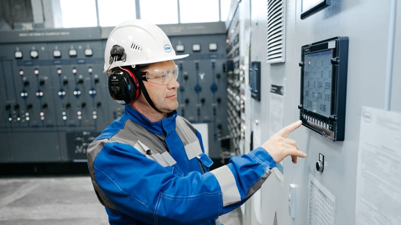 Technicien en équipement de sécurité travaillant sur un panneau de contrôle industriel à l'intérieur.