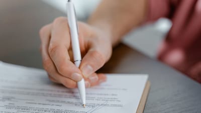 Vue détaillée d'une main écrivant une signature sur un document officiel avec un stylo à bille.