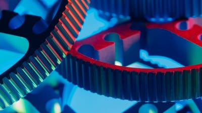 Gros plan macro d'engrenages métalliques imbriqués, mis en valeur par un éclairage bleu et rouge éclatant.