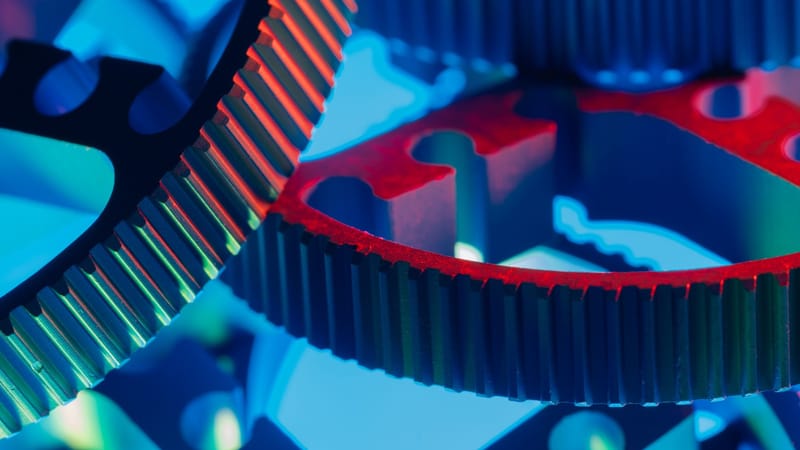 Gros plan macro d'engrenages métalliques imbriqués, mis en valeur par un éclairage bleu et rouge éclatant.