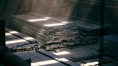 La lumière du soleil filtrant à travers un entrepôt industriel met en valeur des poutres métalliques empilées.