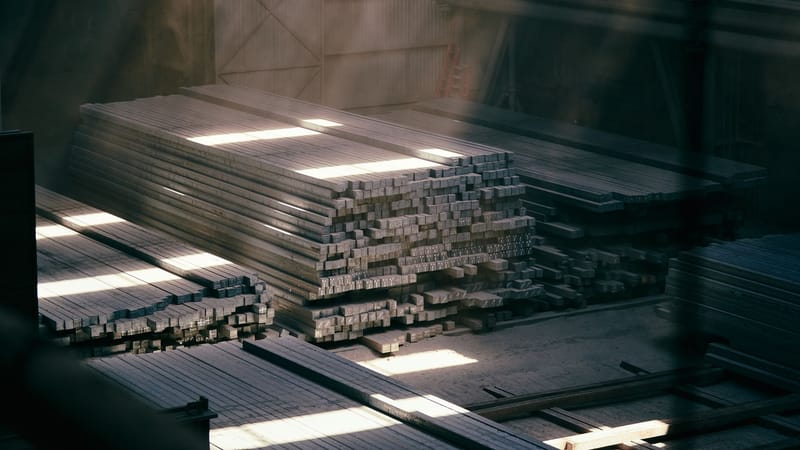 La lumière du soleil filtrant à travers un entrepôt industriel met en valeur des poutres métalliques empilées.