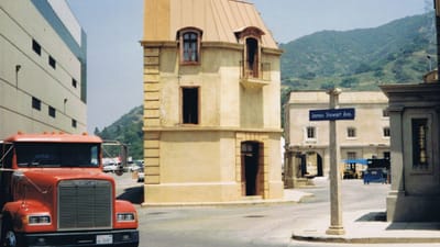 Un bâtiment rustique sur un plateau de studio de cinéma avec un camion garé près d'un fond de montagne.