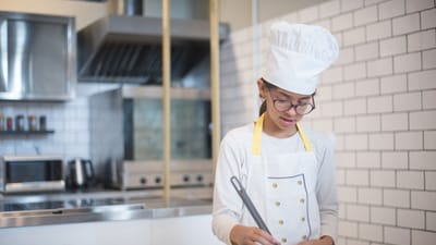 Une jeune fille en tenue de chef cuisinant dans une cuisine moderne avec une poêle.