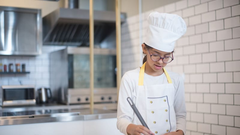 Une jeune fille en tenue de chef cuisinant dans une cuisine moderne avec une poêle.