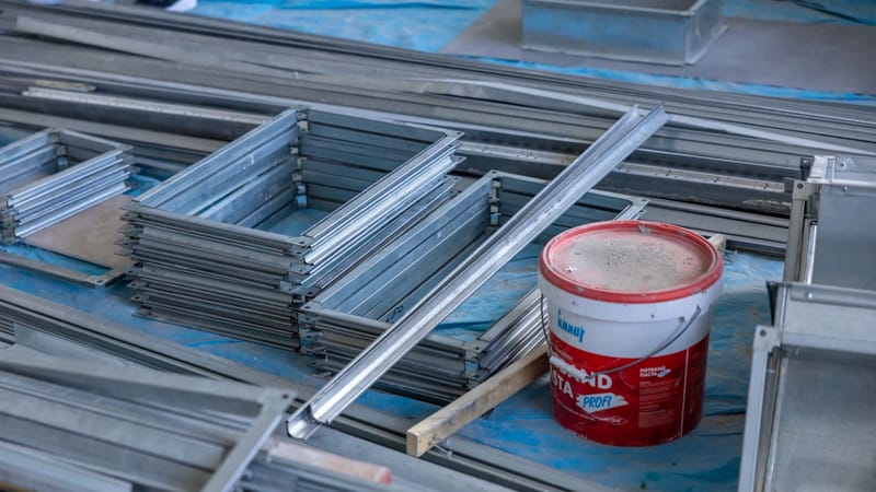 Des piles de cadres en métal et un seau de peinture à l'intérieur d'un site de construction mettant en avant les matériaux de construction.