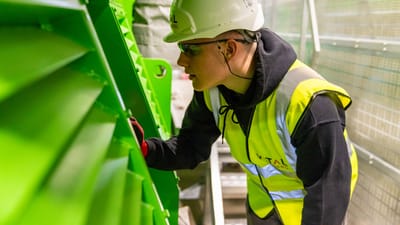 Un travailleur en gilet de sécurité et casque inspectant des machines industrielles.
