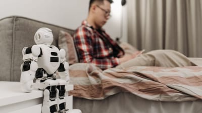 Une chambre moderne avec un robot sur une table de chevet et un homme assis sur un lit.