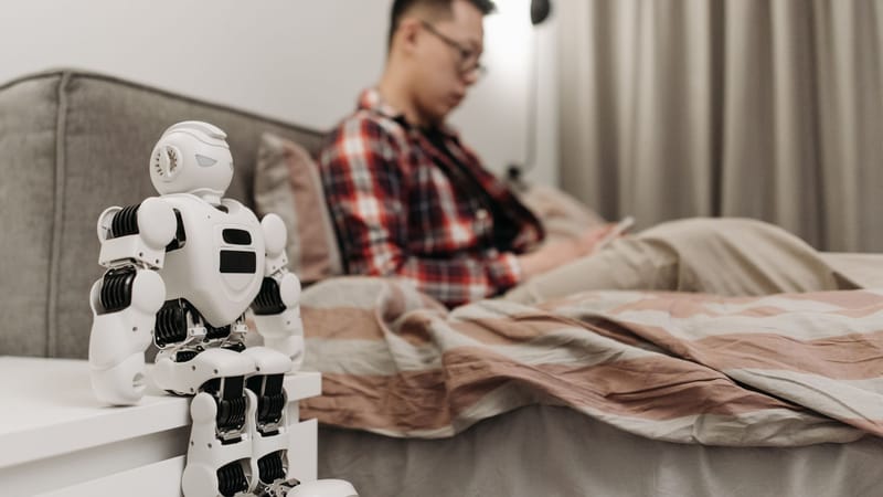 Une chambre moderne avec un robot sur une table de chevet et un homme assis sur un lit.