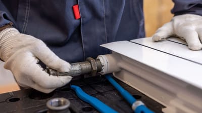 Gros plan d'un plombier installant un tuyau de radiateur à l'aide d'outils spécialisés.