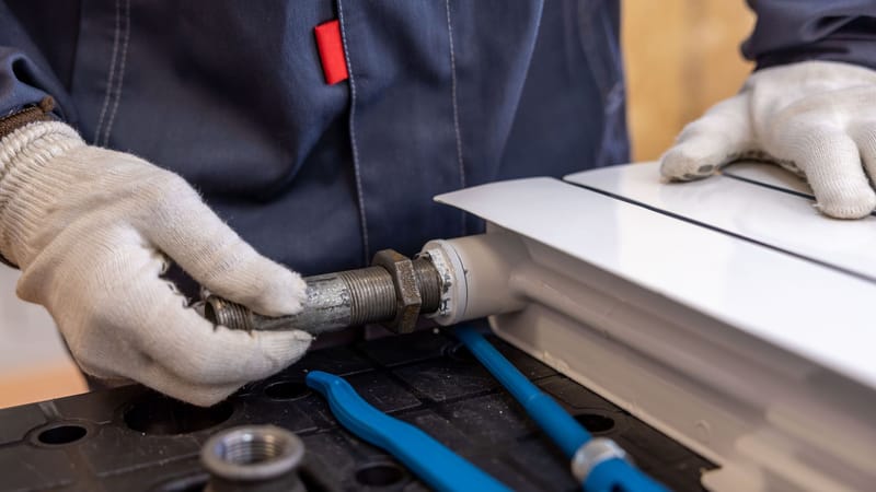 Gros plan d'un plombier installant un tuyau de radiateur à l'aide d'outils spécialisés.