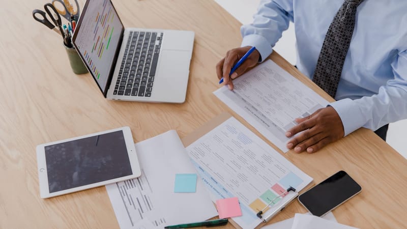 Vue en plongée d'un homme d'affaires travaillant à un bureau avec un ordinateur portable, une tablette et des documents.