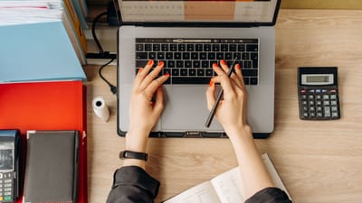 Vue de dessus des mains tapant sur un ordinateur portable sur un bureau avec des dossiers et une calculatrice.