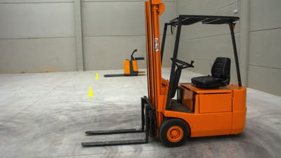 Un chariot élévateur orange dans un entrepôt spacieux avec des sols en béton et peu d'équipement.