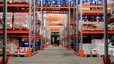 Un vaste entrepôt industriel avec des étagères bien fournies et un travailleur en équipement de protection.