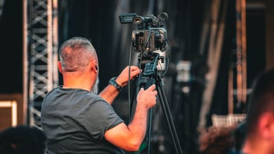 Un caméraman professionnel utilisant une caméra vidéo sur trépied lors d'un événement en plein air, capturé de derrière.