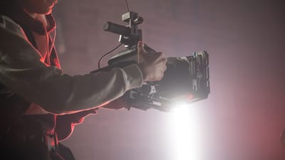 Caméraman utilisant un Easyrig pour filmer dans un studio faiblement éclairé avec des effets de projecteur.