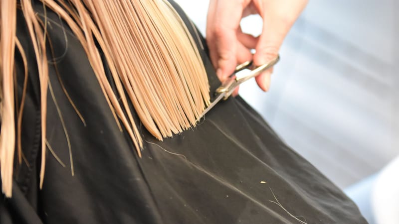 Coiffeur professionnel coupant des cheveux blonds avec des ciseaux dans un salon en gros plan.