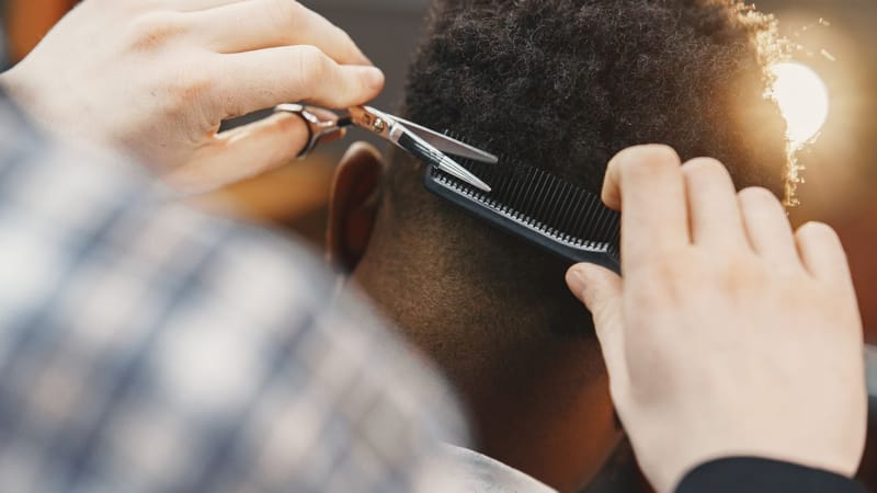 Gros plan sur un coiffeur professionnel taillant une coiffure afro avec des ciseaux et un peigne.