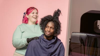 Coiffeuse stylisant joyeusement les cheveux de sa cliente dans un studio moderne, mettant en avant la diversité et le professionnalisme.