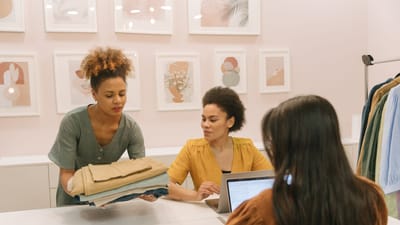 Trois femmes travaillant ensemble dans une boutique moderne, discutant de mode et de stratégies commerciales.