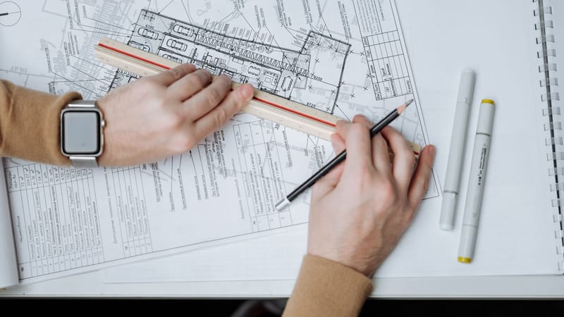 Un architecte utilise une règle et un crayon sur des plans, mettant en valeur son espace de travail et sa planification.
