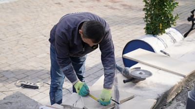 Un ouvrier du bâtiment mesurant des carreaux à l'extérieur avec des outils de précision.