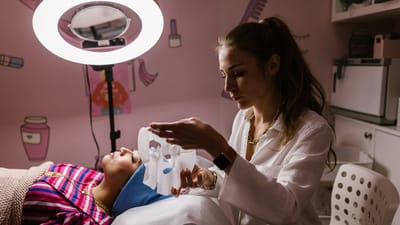 Esthéticienne appliquant un masque en tissu sur une femme dans un salon de beauté pour un traitement facial rajeunissant.