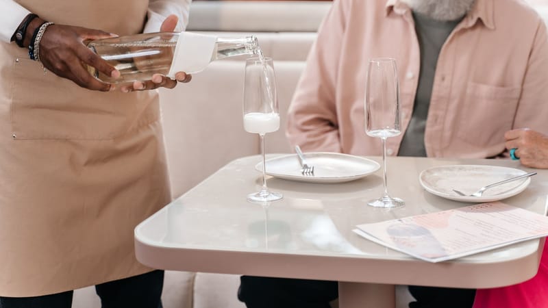 Un serveur versant une boisson pour un homme âgé assis à une table de restaurant. Accent sur l'hospitalité.