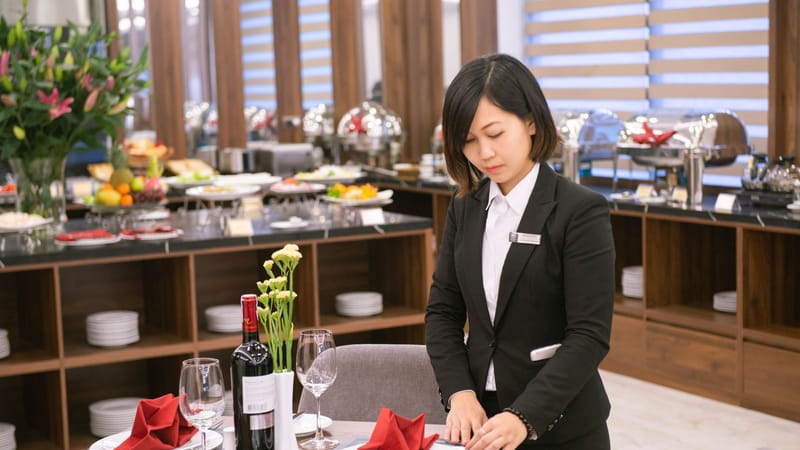 Serveuse asiatique mettant en place une table élégante dans un restaurant à Hanoi, créant une expérience gastronomique formelle.