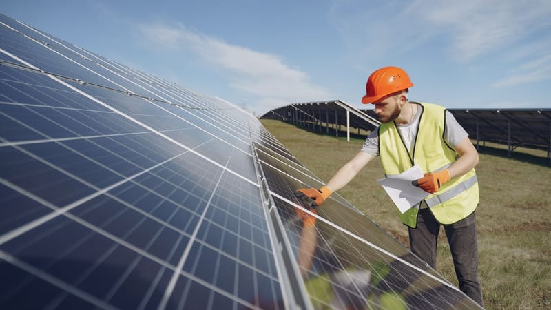 Technicien en EPI inspecte des panneaux solaires dans un champ d'énergie renouvelable, favorisant la durabilité.